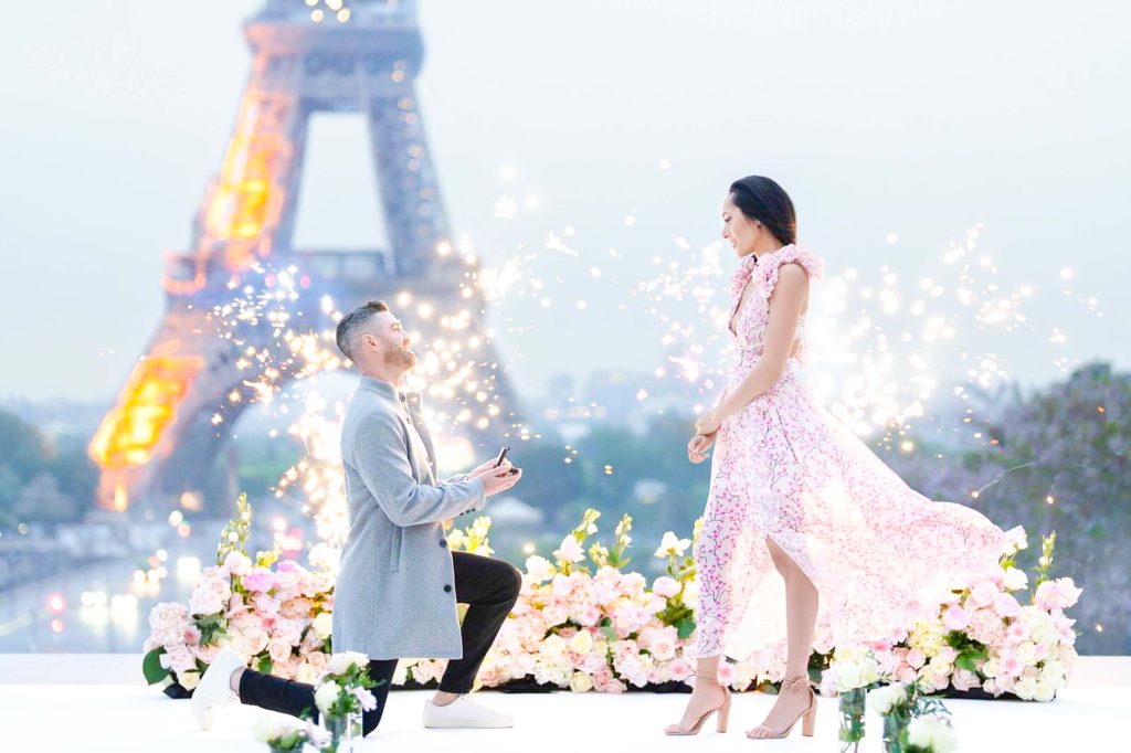 Luxurious Trocadéro proposal setup with vibrant white rose bushes, an elegant white carpet, and fireworks illuminating the Eiffel Tower view.