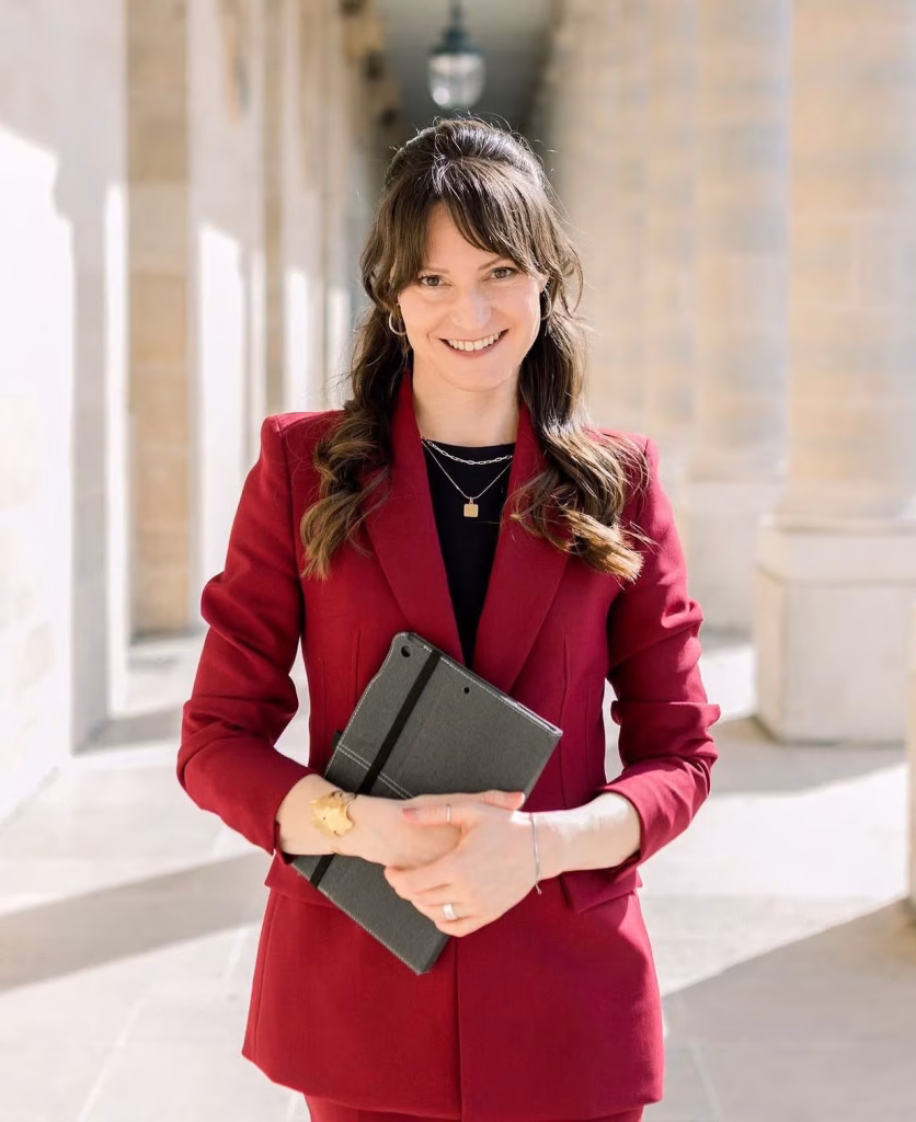 Laura, Paris elopement officiant, smiling in a red suit holding a ceremony book in a stone arcade in Paris